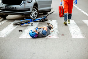 Road accident with injured cyclist lying on the pedestrian crossing, medic going to apply first aid
