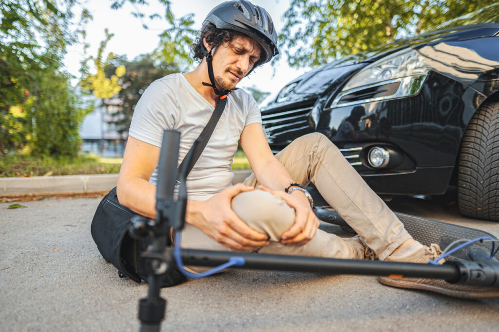 man with helmet holding his knee after a scooter accident